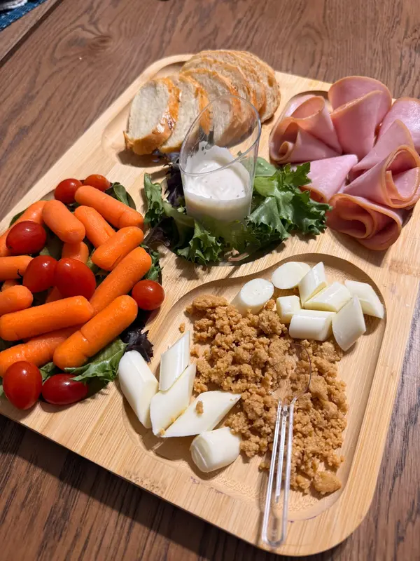 Bamboo tray with sliced homemade bread, ham, salad, baby carrots and cherry tomatoes
