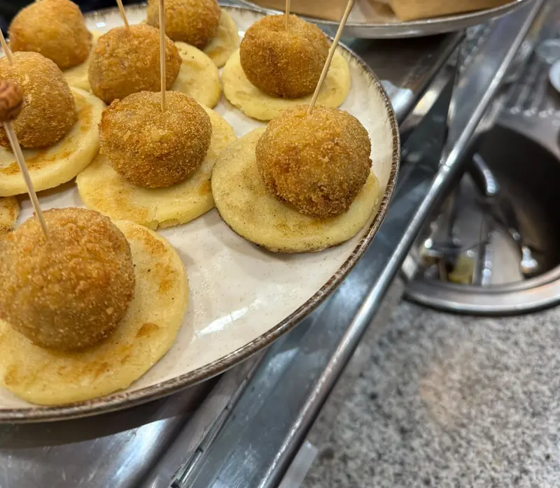 Croquettes on arepa rounds, with patatas bravas in the background