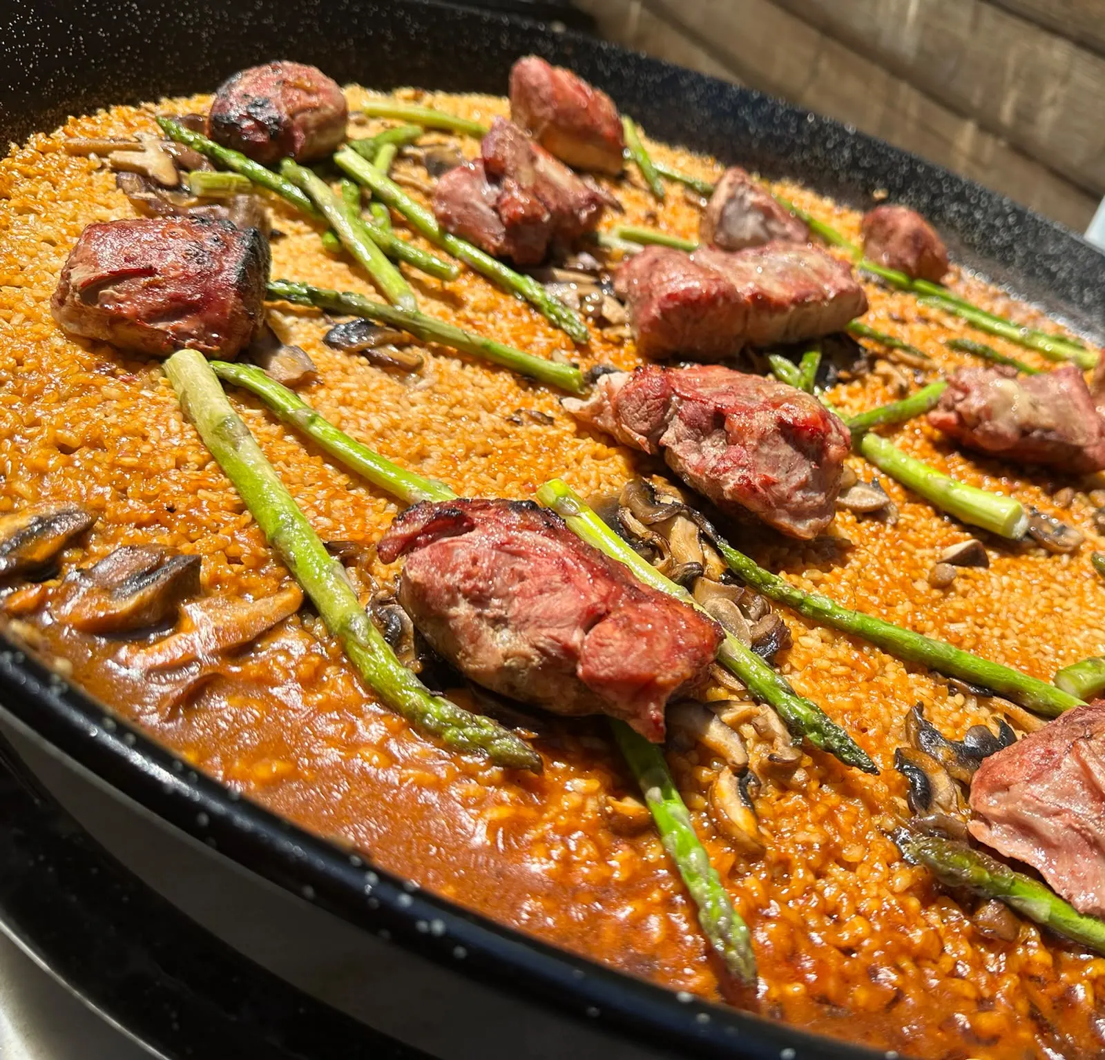 Paella pan of rice with grilled meat, wild asparagus and mushrooms