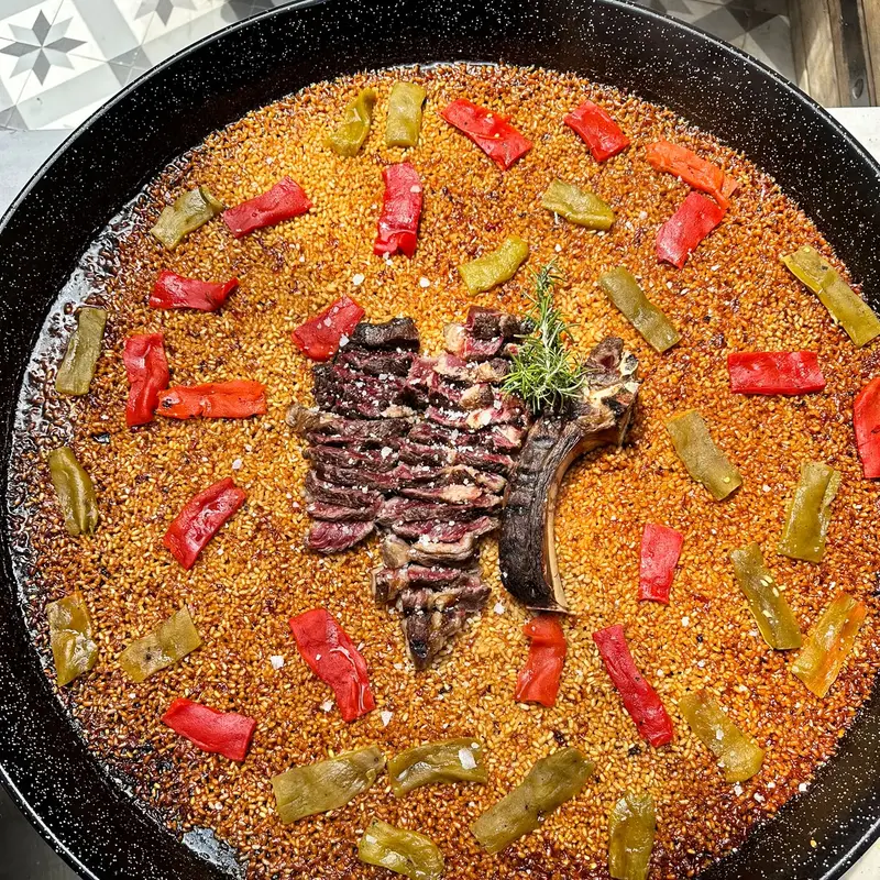 Paella pan from above with sliced ribeye and roasted peppers
