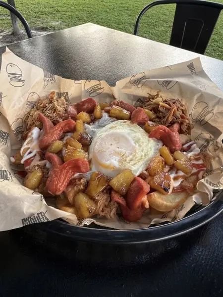 Salchipapa loaded with sausage, pulled pork, grilled pineapple and a fried egg